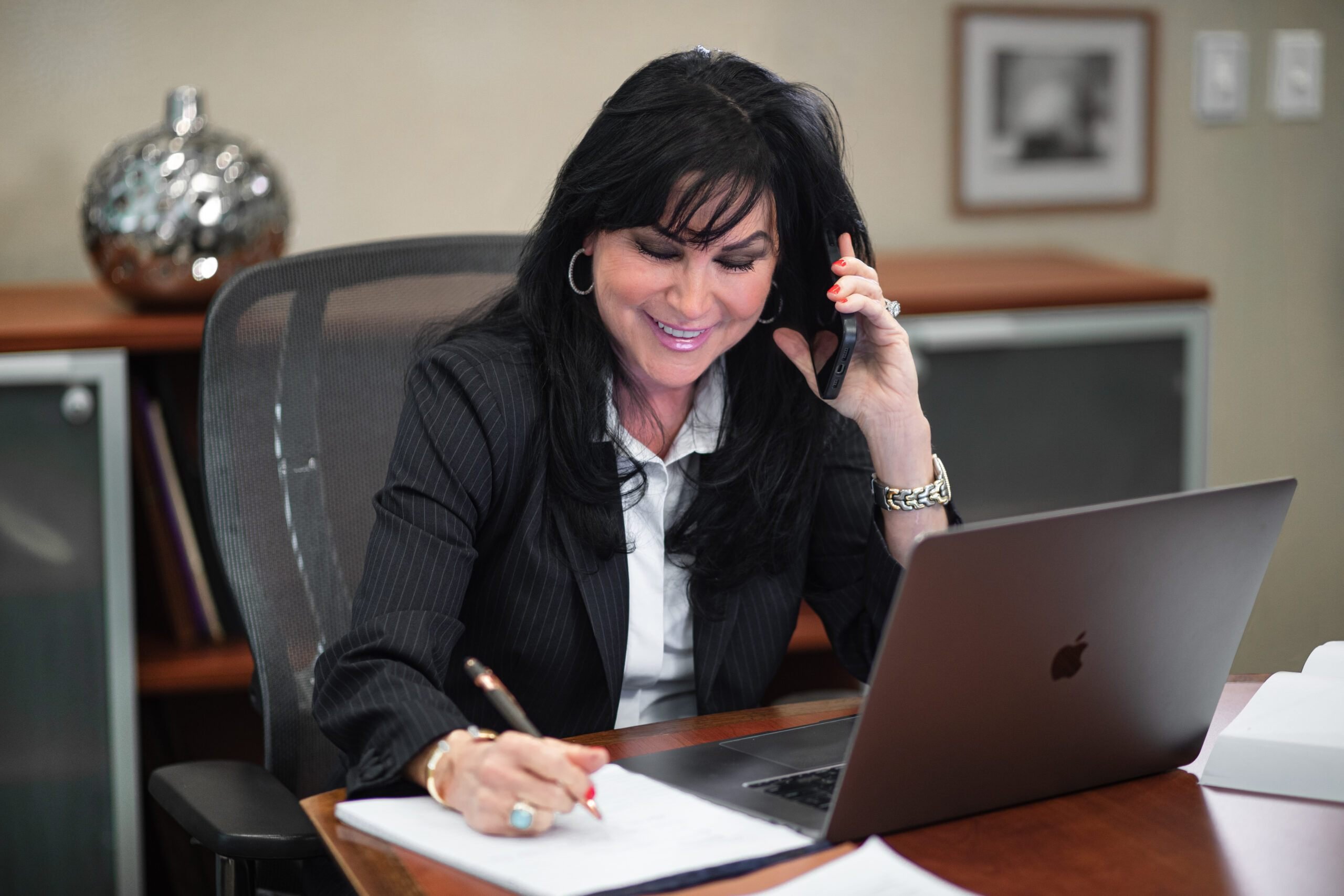 Woman in professional setting taking notes during a phone call